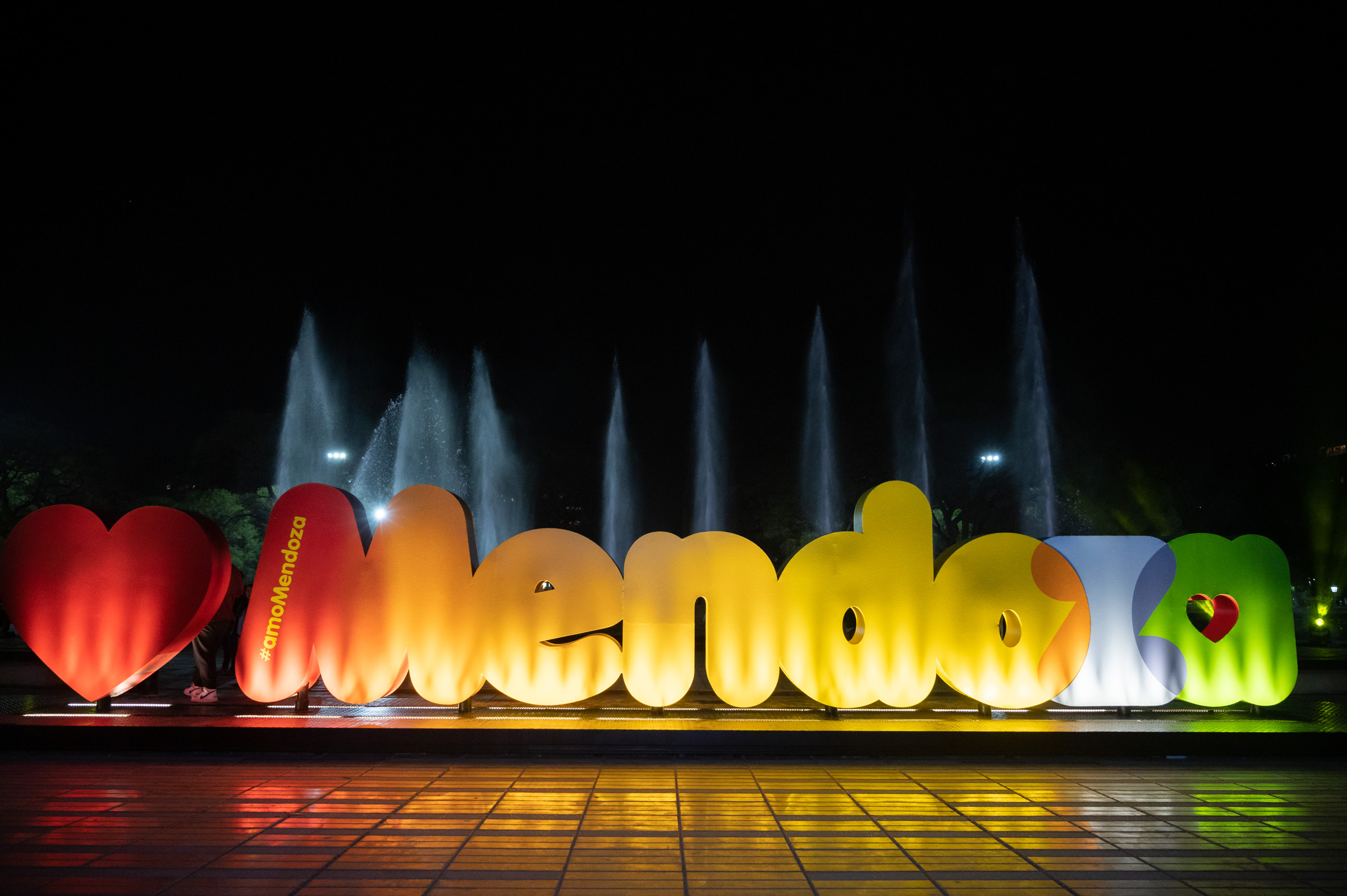 Cartel Mendoza iluminado de noche con fuentes — city tour